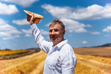 A man in a white shirt is joyfully waving his hat in a vibrant rural landscape under a blue sky.