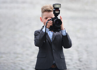 Child photographer holding a camera. Young photographer capturing a picture. Kid playing paparazzi with a DSLR. Boy taking a photograph outdoors. Cute child learning photography. Little journalist.