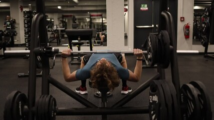 A person is performing a bench press with a barbell in a gym. The workout focuses on building upper body strength, and the gym's clean and professional setting enhances the experience.