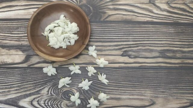 A bunch of White Jasmine or Jasminum sambac flowers in a small wooden bowl on a wooden table.