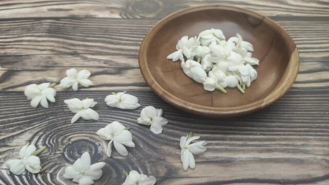 A bunch of White Jasmine or Jasminum sambac flowers in a small wooden bowl on a wooden table.