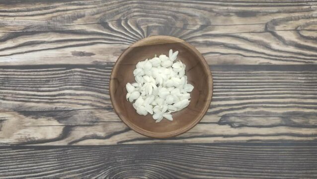 A bunch of White Jasmine or Jasminum sambac flowers in a small wooden bowl on a wooden table.