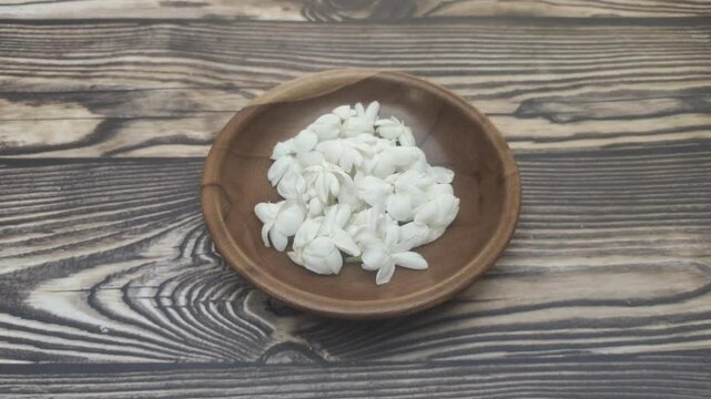 A bunch of White Jasmine or Jasminum sambac flowers in a small wooden bowl on a wooden table.