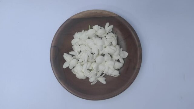 A bunch of White Jasmine or Jasminum sambac flowers in a small wooden bowl on a white background