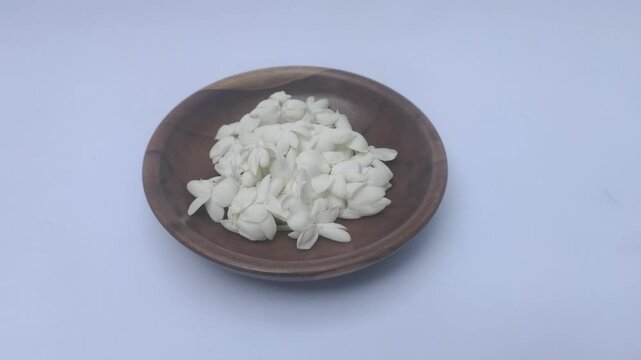A bunch of White Jasmine or Jasminum sambac flowers in a small wooden bowl on a white background