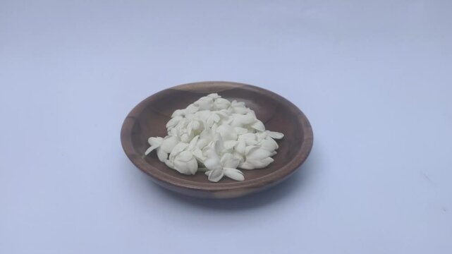 A bunch of White Jasmine or Jasminum sambac flowers in a small wooden bowl on a white background