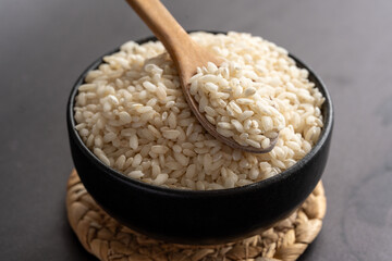 Macro photography of white short grain rice in wooden spoon on dark background. Short white rice in wooden spoon. Closeup photo of rice. 