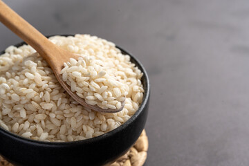 Macro photography of white short grain rice in wooden spoon on dark background. Short white rice in wooden spoon. Closeup photo of rice. 