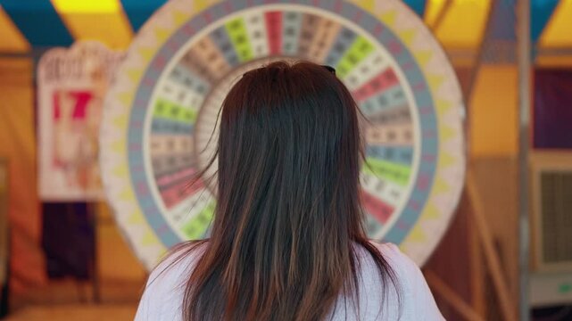 Rear view of a woman playing a spinning wheel luck game at an amusement park. Chance and entertainment concept