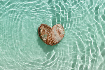 Minimal aesthetic scene, heart from iridescent seashells in waves seawater at sunlight, natural...