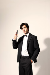 Handsome young man wearing elegant black suit and using smart phone posing over white background. Vertical.