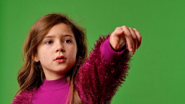 Girl child with shocked face pointing with hand at side and covering face with hands, scared expression, isolated on chroma key green screen studio background mockup.