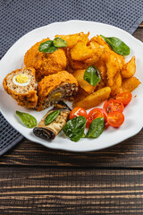 Crispy stuffed chicken with fried potatoes and fresh vegetables on a plate