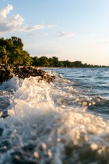 Waves crash on the shore at sunset, with trees in the background; for travel ads