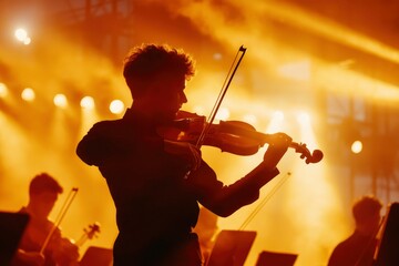 Fototapeta premium Violinist plays at outdoor concert bathed in orange light. Orchestra in background