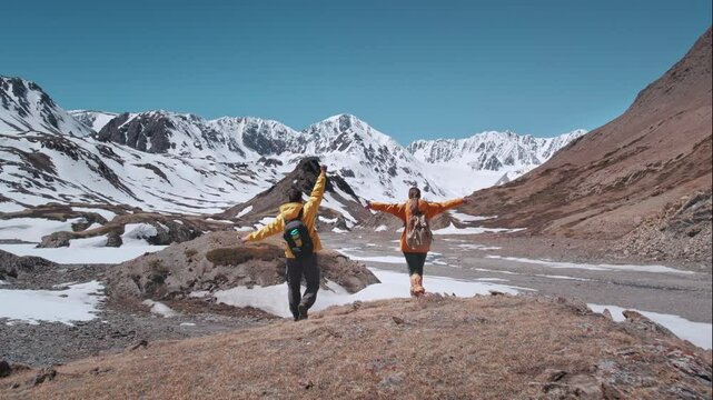 Two happy young hikers tourists finished climb to mountain top and stands with open arms in winner poses