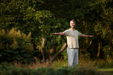 Smile, man and stretching for yoga on grass with mindfulness, spiritual healing and peace at garden. Thinking, male person and warm up muscle with mental health, holistic balance and fitness wellness