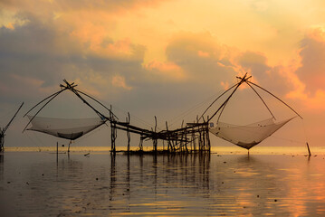 Golden Hour Serenity: Traditional Thai fishing nets silhouetted against a vibrant sunset sky. Perfect for your next travel or nature-themed project.