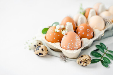 A delicate Easter background with hand-painted eggs in a box on a white table. Easter composition with flowers and feathers