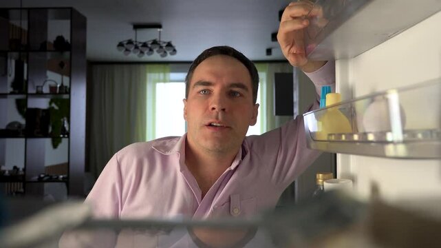 POV point of view from inside refrigerator Caucasian hungry man adult sad upset disappointed male. guy looking for good open empty fridge no food without products. crisis delivery supermarket