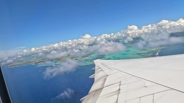 Large airplane climbing after takeoff from Mauritius airport. View from the window above the wing, showing the island, ocean, and low clouds.