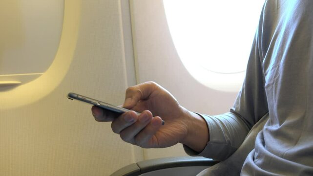 A man is using his cell phone while sitting in a chair. Concept of relaxation and leisure, as the man is focused on his phone rather than his surroundings