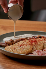 A hearty and delicious plate of potato pancakes (deruny), served with crispy bacon, sauteed mushrooms, and a dollop of sour cream.