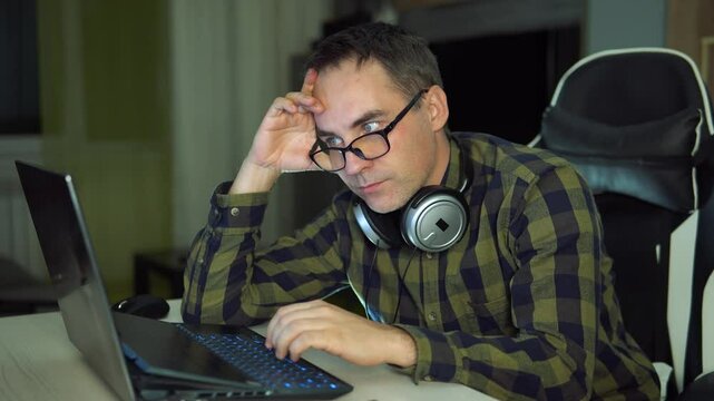 An attentive student in a plaid shirt studies science at home. man holding laptop and looking extremely perplexed on home backdrop. working hard,