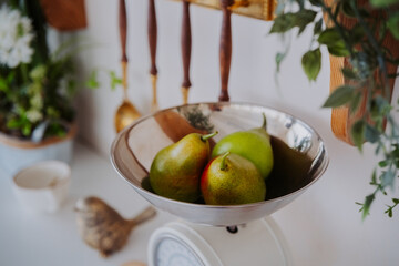 Fresh pears on a kitchen scale surrounded by greenery and utensils