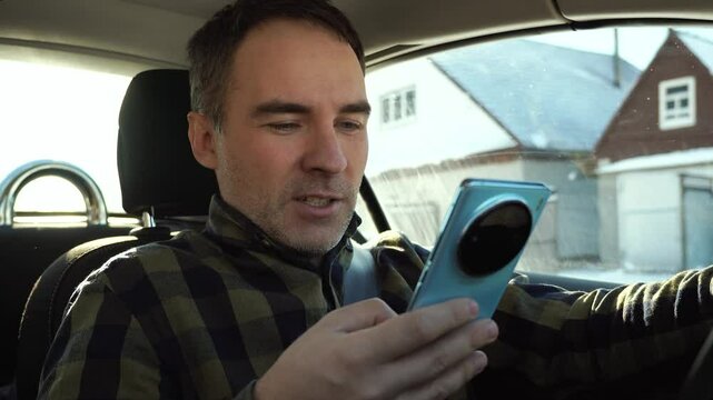 Young driver guy distracted by his phone while in front of the steering wheel, using his smartphone with one hand while driving. Risk and danger situations on the road, violating traffic rules