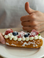 Person is holding a dessert with strawberries and blueberries on top