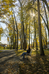 A woman sits on a bench in a park, reading a book