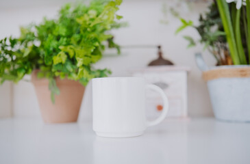 Empty white mug on a table surrounded by greenery and kitchen decor