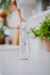 Decorative glass bottle with lace ribbon and greenery in background