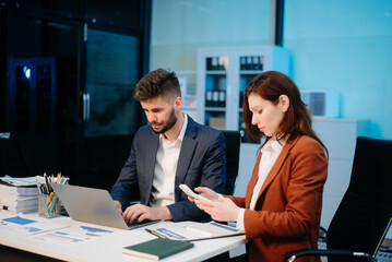 Two office colleagues discuss ideas for a startup project in a modern workspace, using laptops and smartphones