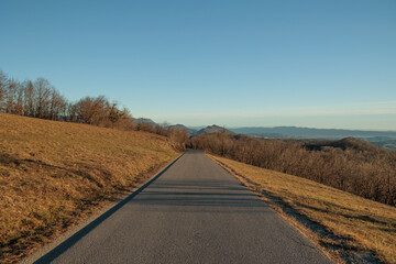 panoramica su di un ambiente naturale collinare in Slovenia, in cima ad una collina, visto da lungo una strada alta, asfaltata, in discesa, in inverno, con cielo sereno