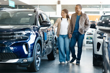 Couple Choosing New Car Together Standing Near Luxury Vehicle In Auto Dealership Showroom. Family...