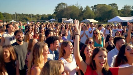 A cheerful crowd at an outdoor music festival during the day, full of energy and excitement.