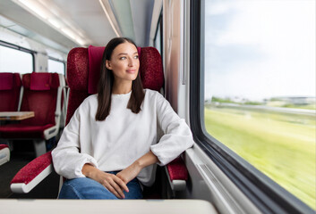 Pensive European woman traveler sitting near window on comfortable chair in express train, looking...
