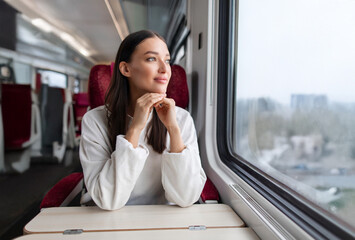 Young beautiful European woman dreaming, looking through the window inside train wagon, enjoying...