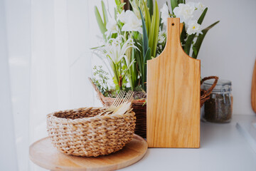 Wooden cutting board and woven basket with greenery in a bright kitchen