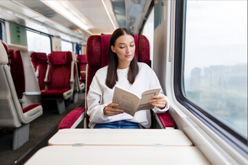 Lady reading book, sitting near window in train, travelling by railway, free space. Travel and...