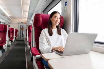 Happy woman freelancer working on her laptop computer riding by train, enjoying trip to another city. Transportation and wireless connection