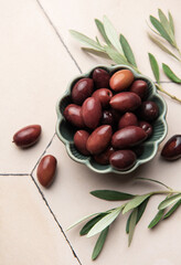 Kalamata olives with olive branches in a green bowl on a tiled surface