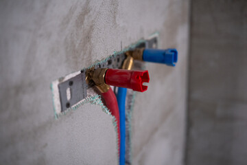Plumbing installation with red and blue connections on unfinished wall surface