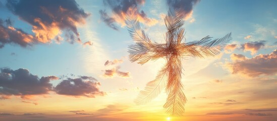 Obraz premium Wire cross adorned with feathers set against a vibrant sunset sky with soft clouds, hues of orange and blue creating a serene atmosphere.