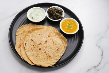 Roti and Sabzi. Indian vegetarian Thali includes bhindi fry, yellow daal tadka, cucumber raita, and chapati or tel paratha. Indian food is served in a plate or thali. Copy Space. healthy Veg Thali