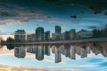 Fototapeta premium City skyline reflects in calm lake surrounded by trees during sunset with vibrant clouds and soft glow