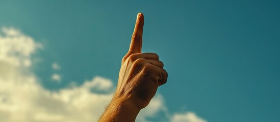 Hand raised with index finger pointing upwards against a blue sky and fluffy white clouds emphasizing hope and inspiration in a sunny environment.