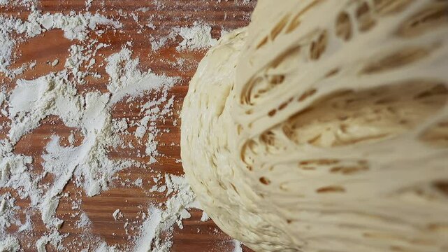 A highly detailed close-up of fermented dough being lifted, revealing an intricate network of air pockets and gluten strands. The dough is elastic and porous, with a well-developed structure